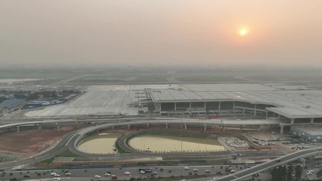 An aerial view of the expansive, modern Terminal 3 at Hazrat Shahjalal International Airport, beautifully framed by winding highway overpasses at dawn.