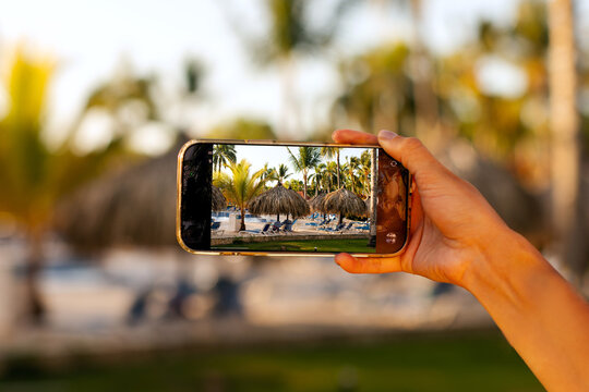 Close up of hand holding smartphone capturing tropical resort scene