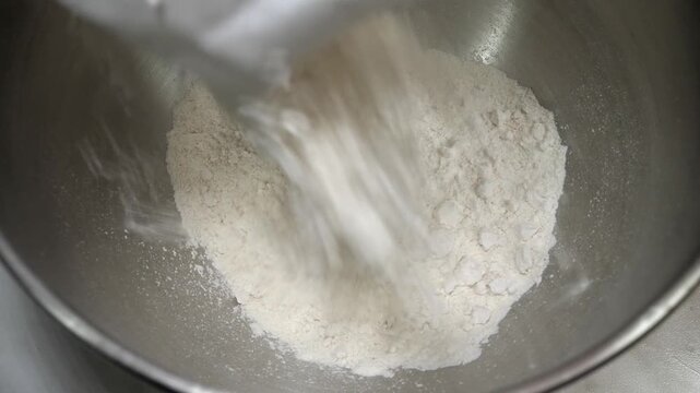 Flour is poured into a bowl as part of homemade cookie preparation. The scene captures a fundamental baking step in a warm and authentic kitchen setting.