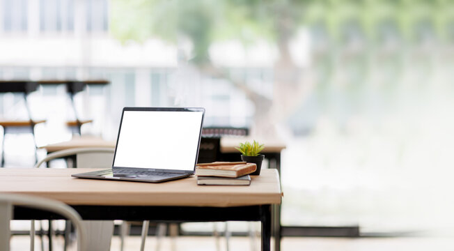 Laptop Computer, notebook, and eyeglasses sitting on a desk in a large open plan office space after working hours White blank screen laptop on modern working desk