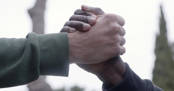 Close-up low angle shot of two men shaking hands, one black and one white. The gesture symbolizes unity, equality, respect and solidarity between different cultures and people.