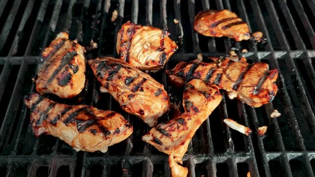 Close-up cinematic chicken grilling on black barbecue grill with flames, smoke and sizzling heat, juicy meat cooking outdoors at summer backyard BBQ with authentic fire ambiance at sunset glow.