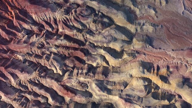 A top-down drone perspective reveals the colorful geological strata of the Painted Desert. The eroded badlands patterns offer a surreal and alien-looking terrain.