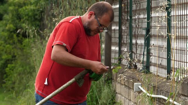 Gardener replacing trimmer line on grass cutter during outdoor work
