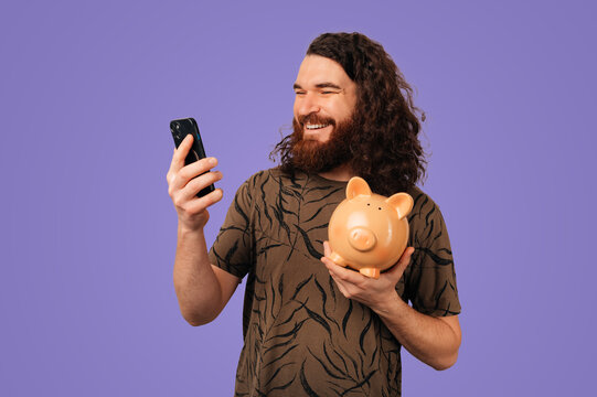 Caucasian Man Holding Piggy Bank And Phone, Checking Finance App For Savings, Fintech Concept With Purple