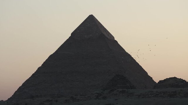Pyramids of Giza at dusk with birds flocking in the evening sky