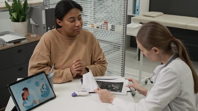 Caucasian fertility doctor examining ultrasound results of African American woman and discussing them with her during IVF consultation