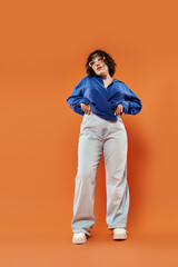 Fototapeta premium Young woman showcases vibrant fashion against a bright orange backdrop, expressing unique style