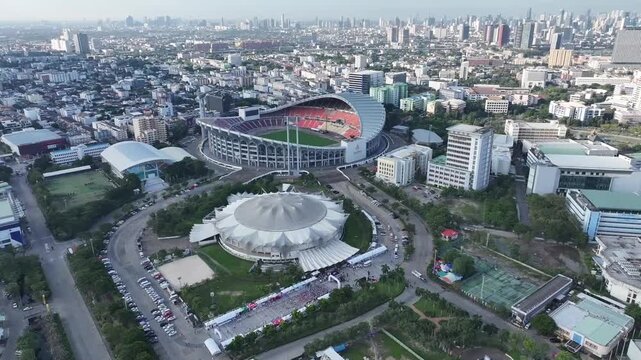 A large sports complex with stadium and facilities appears from above, connected by roads and surrounding city buildings.