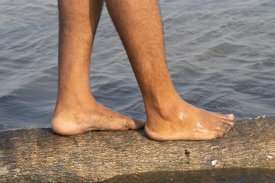 Human feet of an adult male standing barefoot on a decayed tree found in the mid of the lake from backwater