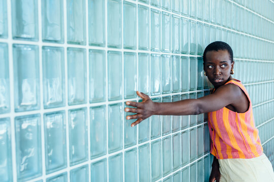Detached Black woman touching glass block wall in minimalist space