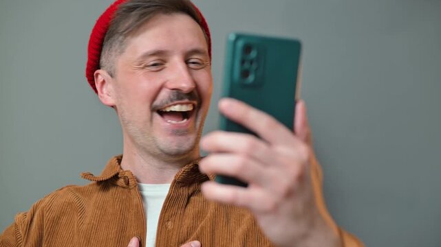 A man in his 30s with light skin and a mustache interacts with his smartphone, showing various expressions in a home environment