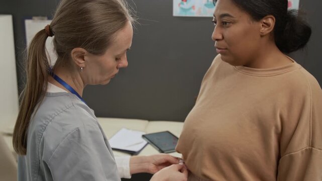 Tilt up zoom out view of Caucasian female gynecologist measuring waist of African American woman during pre-pregnancy checkup in clinic