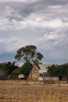 Dilapidated stone farmhouse with corrugated iron roof under a dramatic cloudy sky