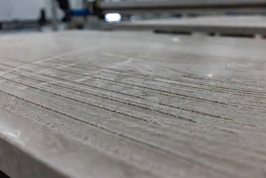 Close-up of parallel grooves on a light-colored stone slab, indicating industrial processing.
