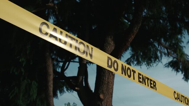 Yellow caution tape do not enter angled against trees background daytime shows restricted access area safety and perimeter control in outdoor environment
