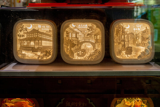 Three illuminated paper-cut light boxes depicting Suzhou landmarks including Humble Administrator's Garden and Pingjiang Road, glowing with warm golden light.