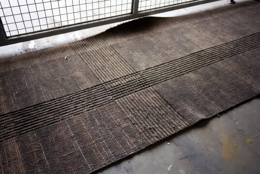 Textured woven natural fiber mat with horizontal ribbed pattern on concrete floor