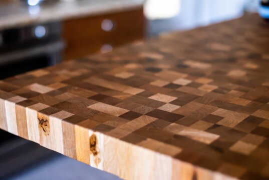 Detailed close-up of a rich, warm, end-grain butcher block countertop with a blurred kitchen background.