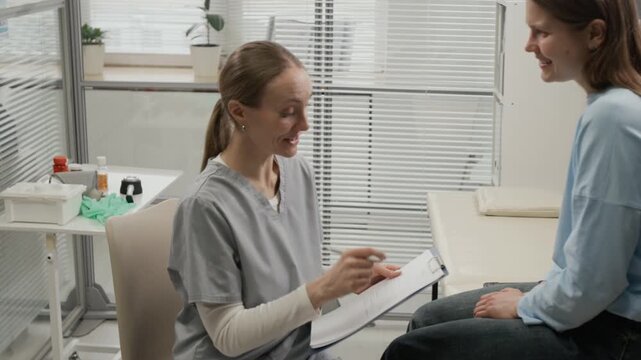 Positive reproductive specialist speaking with young woman sitting on medical couch, and taking notes while patient visiting fertility clinic
