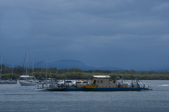Vehicle ferry crossing river in sun, clouds and boats in background