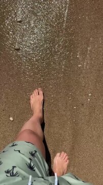High angle of an unrecognizable man standing on the sand and starting to walk into waves