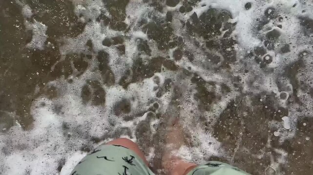 High angle of an unrecognizable man standing on the sand and starting to walk into waves