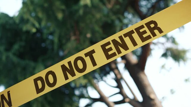 Yellow caution tape do not enter angled against trees background daytime shows restricted access area safety and perimeter control in outdoor environment
