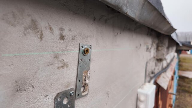 Professional builder using an electric screwdriver to tighten a long screw into a metal bracket mounted on a concrete wall, representing a close-up of house construction or renovation work