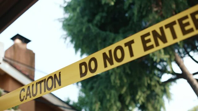 Yellow caution tape do not enter angled against building and trees daytime shows restricted access area safety and perimeter control in outdoor environment
