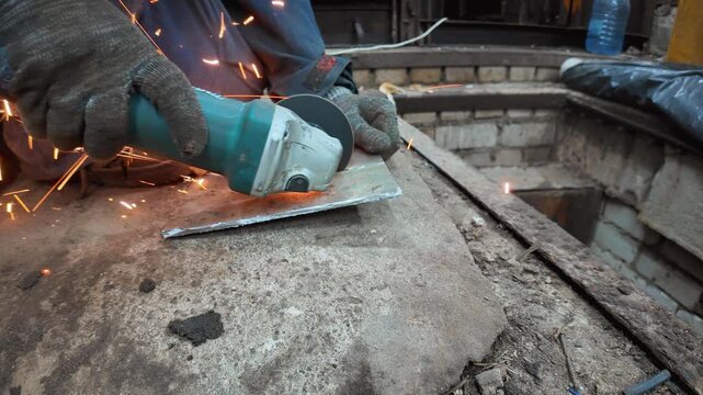Professional craftsman in protective gloves using an angle grinder for cutting a metal sheet, with bright sparks flying during the industrial metalworking process in a workshop