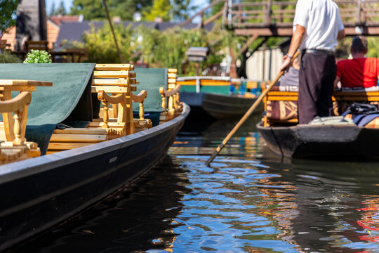 Traditional wooden boat Spreewald canal benches guide paddling long oar tourist relax calm water. Bright sunlight reflections ripples highlighting summer travel atmosphere picturesque rural landscape