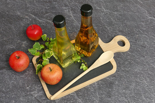 Fresh apples with apple cider vinegar and a wooden spoon on a rustic board.