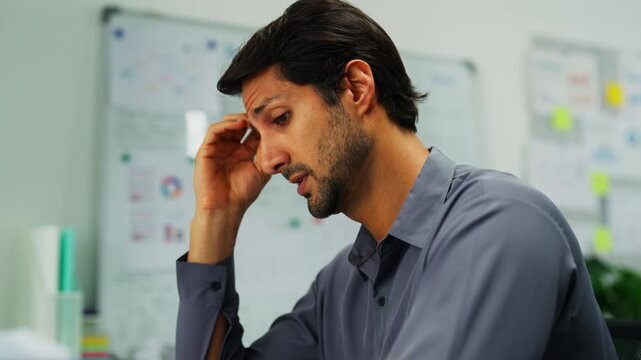 Man alone in office, overworked and frustrated by deadlines, multitasking between computer and documents under pressure.