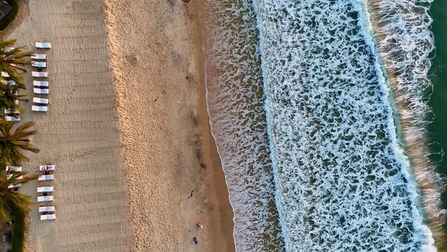 Aerial drone view of waves on a sandy beach with lounge chairs in Mui Ne, Vietnam