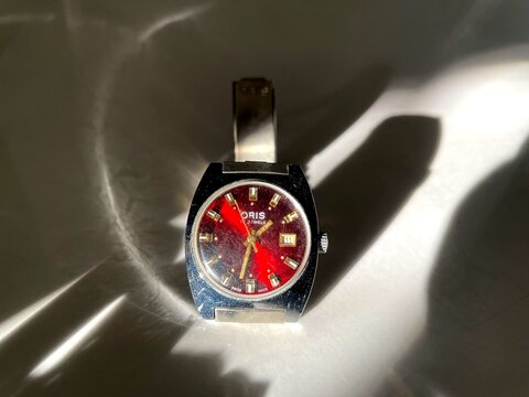Vintage Oris 17 Jewels watch with a striking red dial and metallic band, photographed in dappled sunlight, classic timepiece, retro style, luxury accessory, collectible item, horology, elegant de
