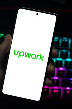 Punta Arenas, Chile &ndash; April 30, 2026: Close-up of the Upwork freelancing platform logo on a mobile phone screen held by a person over a dark desk with glowing RGB keyboard lights