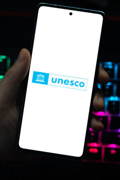 Punta Arenas, Chile &ndash; April 30, 2026: A person holding a smartphone displaying the blue and white UNESCO logo on its screen with a vibrant, colorfully backlit mechanical keyboard in the background