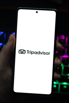 Punta Arenas, Chile &ndash; April 30, 2026: A hand holding a smartphone displaying the Tripadvisor owl logo on its screen with a vibrant, colorfully backlit mechanical keyboard in the background