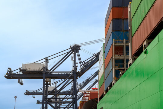 Huge mobile cranes load a green cargo ship with colorful shipping containers at the Port of San Antonio in Chile. The industrial scene shows the scale of international maritime trade.