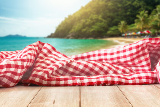 island Picnic Fabric on Wooden Table at Beach &ndash; Summer Background with Checkered Cloth and Coastal Vibes