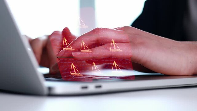 Hands are typing on a laptop with warning symbols displayed on the screen in a bright workspace during daytime.