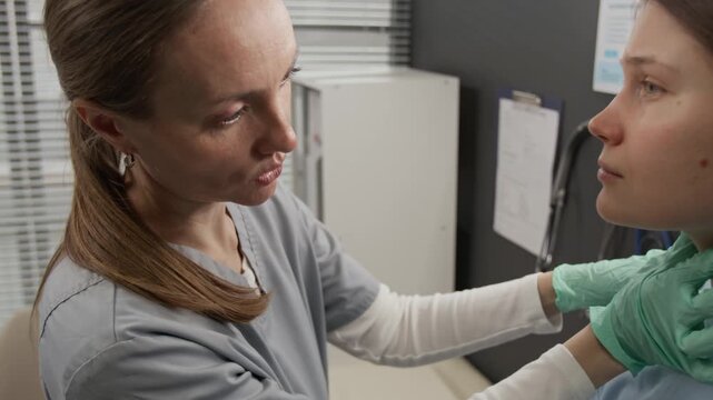 Close-up view of female endocrinologist palpating neck of young woman while examining her lymph nodes during appointment