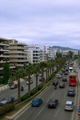 Obraz premium Urban street with palm trees and active traffic, cars and public transport moving along a multi-lane road. Modern residential buildings and hills in the background. Concept of city life, transportatio