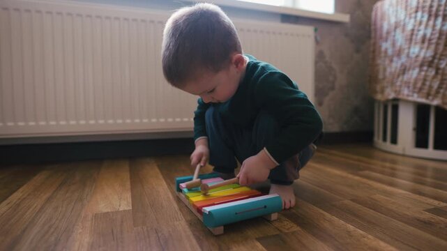 Little boy playing a colorful wooden xylophone on the floor at home, audio included