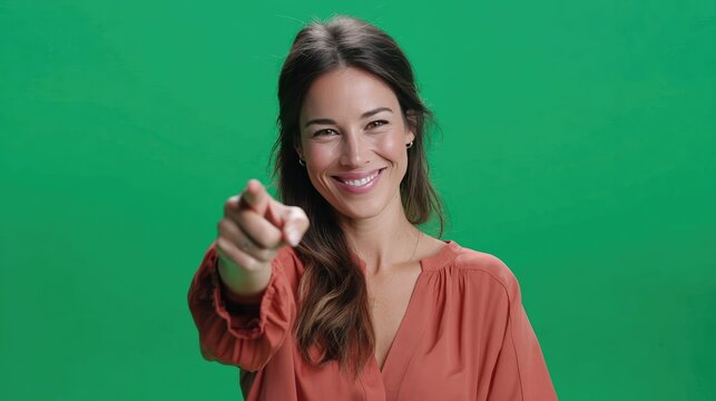 Confident Pointer: A woman exudes confidence as she points directly towards the viewer with a knowing smile, set against a vibrant green backdrop, making an unmistakable declaration of empowerment.