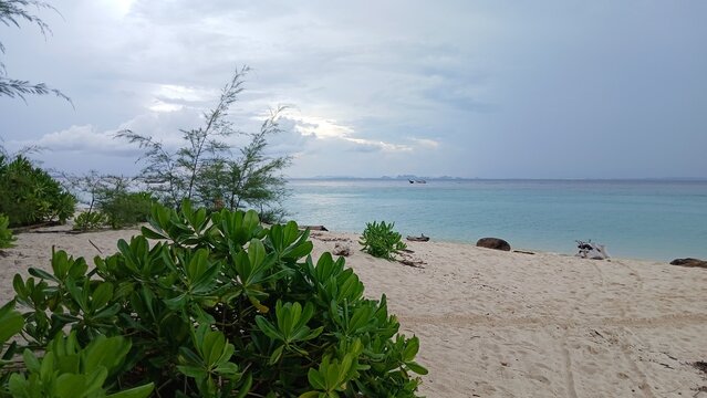 Scenic landscape of Poda Island beach with green coastal shrubs and turquoise ocean under a cloudy sky, Krabi, Thailand