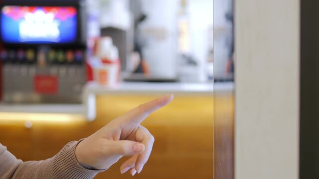 Hand points toward blurred beverage station. Background shows vending machines and counters. Focus remains on finger gesture only. No animals or plants visible. Scene suggests casual indoor setting