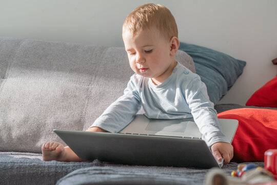 Toddler using computer at home, concept of modern parenting and innovation.
