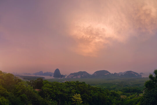 Panorama view majestic limestone formations rise above emerald waters fringed by winding mangroves, with a bustling coastal village visible at orange mammatus clouds sunset.